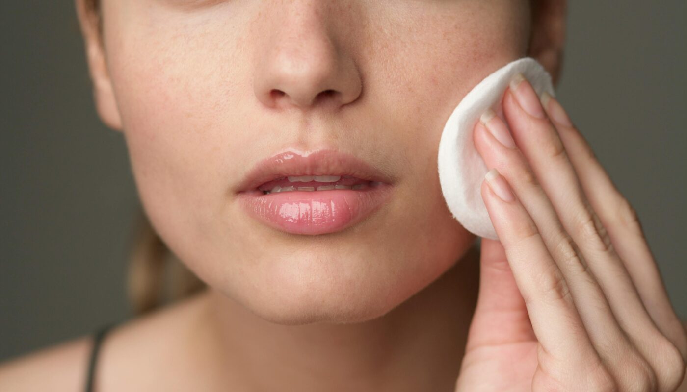 Young woman using a cotton pad for skincare, highlighting beauty routine.