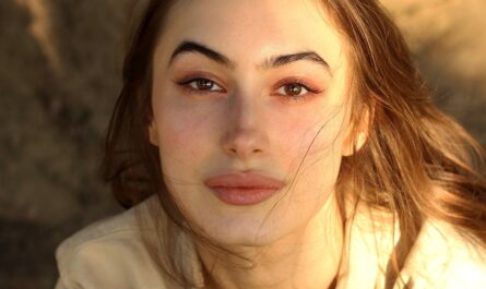 Portrait of a young woman with serene expression, bathed in warm sunlight outdoors.