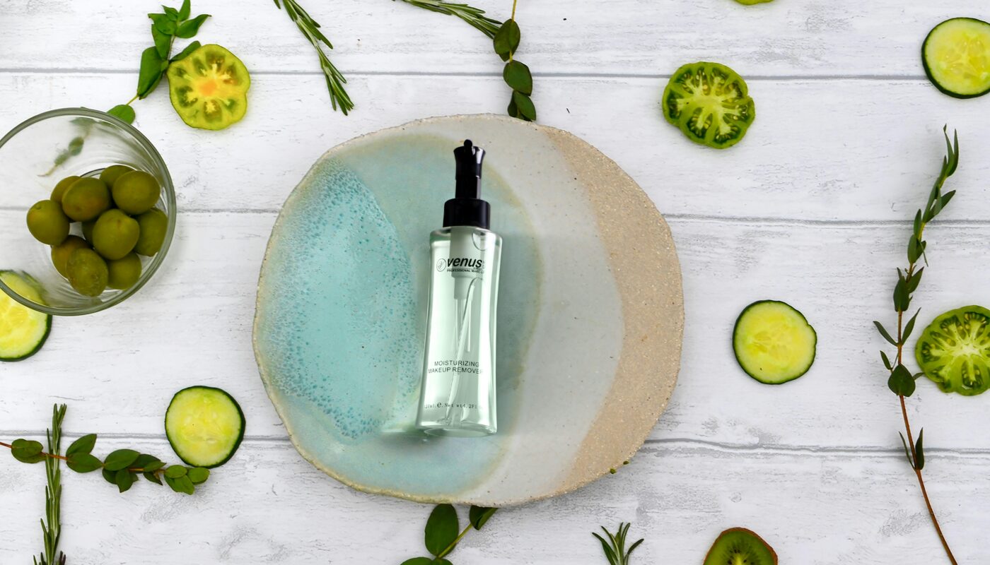 Flat lay of a natural skincare serum surrounded by fresh cucumber slices and herbs on a wooden table.