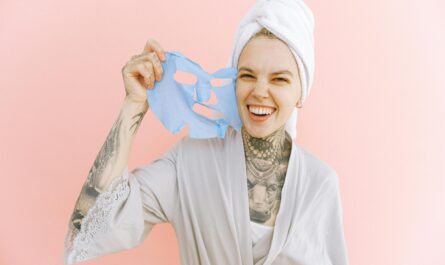 Happy woman holding a blue face mask, wrapped in a towel and smiling brightly.