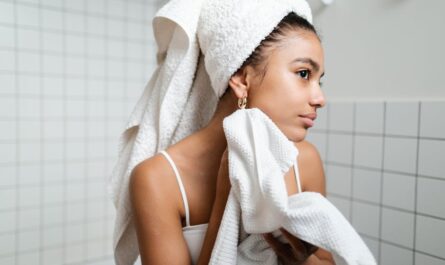 Young woman drying face with towel during morning skincare routine in a modern bathroom.